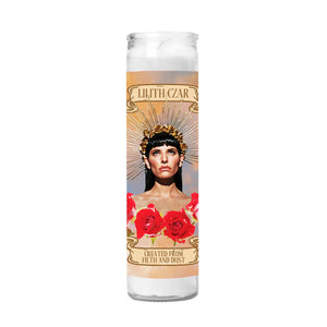 Tall, skinny candle on a white background. The candle has a banner that says Lilith Czar and below that is a photo of Lilith looking up wearing a flower crown and spiked headband with roses around her chest.  There is a banner at the bottom that says Created from filth and dust. 